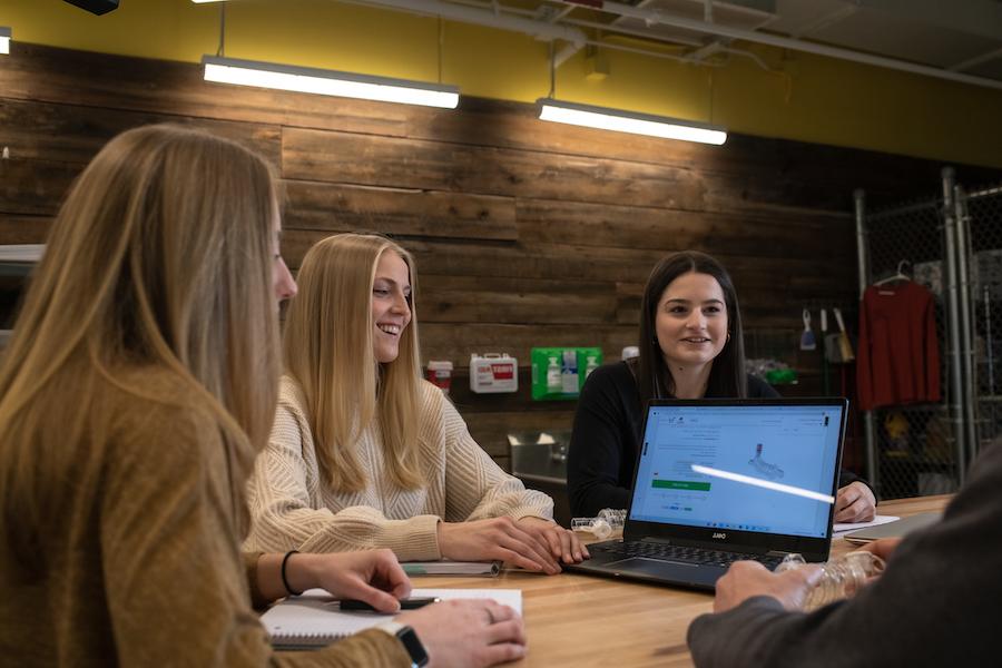 Three female students around a table and computer at Clarkson University.